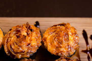 Japanese maki rolls baked with cheese and sprinkled with sauce. Sushi on a wooden plank. Seafood menu on black background