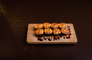 Japanese maki rolls baked with cheese and sprinkled with sauce. Sushi on a wooden plank. Seafood menu on black background
