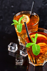 Two glasses with cold traditional iced tea with lemon, mint leaves and ice cubes.