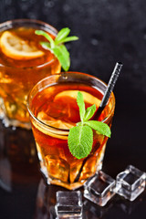 Two glasses with cold traditional iced tea with lemon, mint leaves and ice cubes.