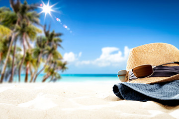 Fototapeta na wymiar Summer sunglasses with hat on sand and blue towel. Free space for your decoration. Blurred background of beach with palms and ocean 