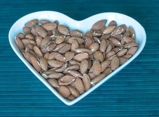 Nuts arranged in heart  on background. Healthy Food image close up almond on the cup plate. Love Texture on top view mock up