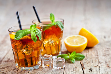 Traditional iced tea with lemon, mint leaves and ice cubes in glasses on rustic wooden table.