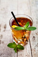 Traditional iced tea with lemon, mint leaves and ice cubes in glass on rustic wooden table