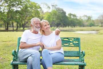 elderly couple with white shirt and blue jean sitting and embracing in park during summer time on wedding anniversary day