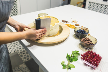 Confectioner smooths white cream on a biscuit cake with a cooking spatula. The concept of homemade pastry, cooking cakes.