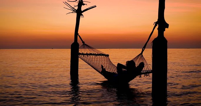 Silhouette of a man relaxing in a hammock during a tropical sunset
