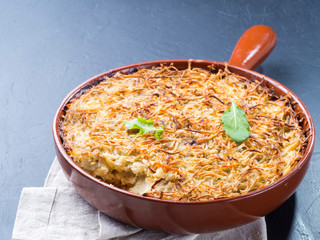 Close up view of appetizing potato casserole with fish, eggs and cream. Potato casserole in serving baking pan on dark concrete background