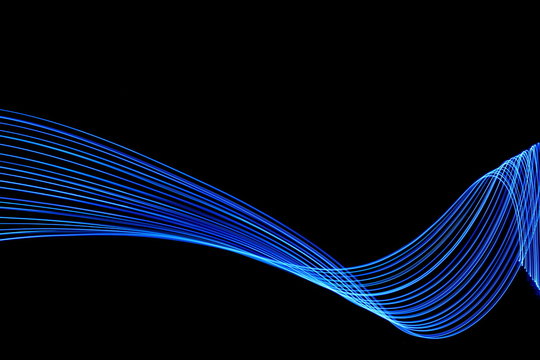 Long exposure, light painting photography.  Vibrant abstract streaks of electric blue color against a black background.