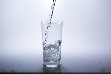 Pour clean drinking water into the glass on the table. Close-up.