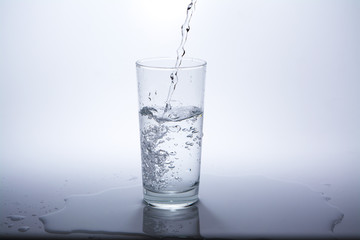Pour clean drinking water into the glass on the table. Close-up.