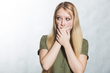 Surprised young woman covers mouth in shock.