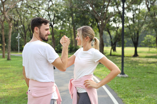 image of young caucasian couple in white and pink sport dress with smiling and arm wrestling challenge in the park with green tree in nature