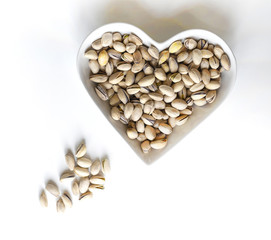 Nuts arranged in heart  on background. Healthy Food image close up pistachios on the cup plate. Love Texture on white grey table top view mock up