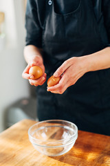 Female chef cracking eggs into a glass bowl