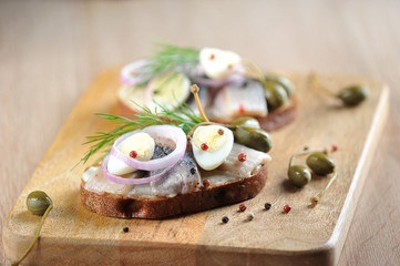 Sandwiches with herring, onions, capers and quail eggs. Traditional dutch snack. Light wooden background. Close-up. Macro shooting. 