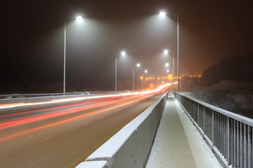 Fototapeta na wymiar winter on the bridge by the light of lanterns light fog and light from passing cars