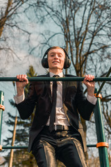 businessman in headphones pulls himself up on a sports horizontal bar. modern young man. Startup...