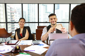 2 caucasian businessmen having meeting with asian businesswoman. They use computer with chart on screen and company graph summary report on table with coffee cup and calculator beside while holding ho