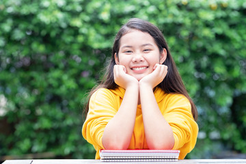 Relaxed schoolgirl primary student smiling and resting her chin in her hands with colorful notebooks