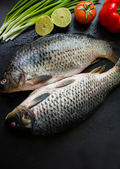 Fresh carp on a dark background with greens and vegetables.