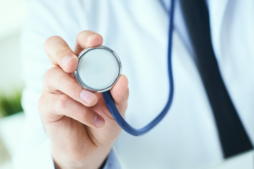 Close up of a doctor's hand, holding a stethoscope outstretched towards the viewer. Medic shop or...