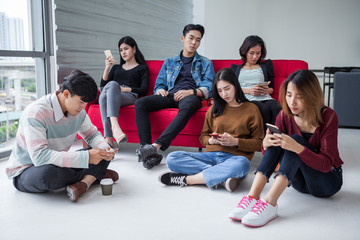 A lonely one man in Group of asian students using smartphone checking social networks online . young people with social media . Phubbing . team ignore. looking out