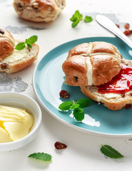 Hot cross buns in blue plate served with butter, strawberry jam and cup of tea