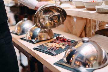 Meat slicing on a plate. The waiter holds the metal lid from the plate open.