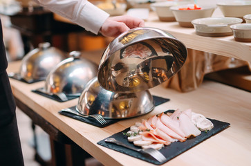 Meat slicing on a plate. The waiter holds the metal lid from the plate open.