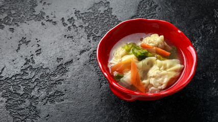 Pork Wonton dumpling soup with vegetables in bowl.