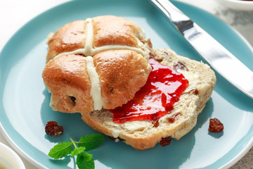 Hot cross buns in blue plate served with butter, strawberry jam and cup of tea