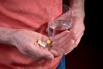 Male holding pills in hand and glass of water