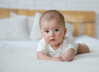 The baby lies on his stomach and looks at the camera. The child is resting on the bed