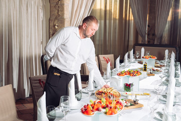 Waiter serving table in the restaurant preparing to receive guests.