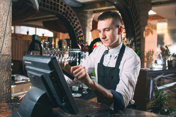 small business, people and service concept - happy man or waiter in apron at counter with cashbox...