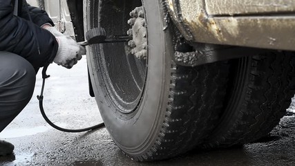 The pump inflates the dirty wheel in the rain in natural light Inflatable tyre compressor with black hose and external pressure sensor in rainy weather
