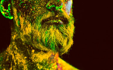 Concept. Portrait of a bearded man. The man is painted in ultraviolet powder.