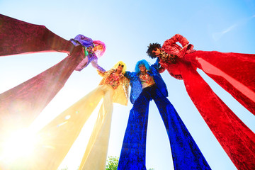 Young people on stilts posing against the blue sky.