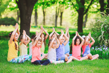 A large group of children engaged in yoga in the Park sitting on the grass.