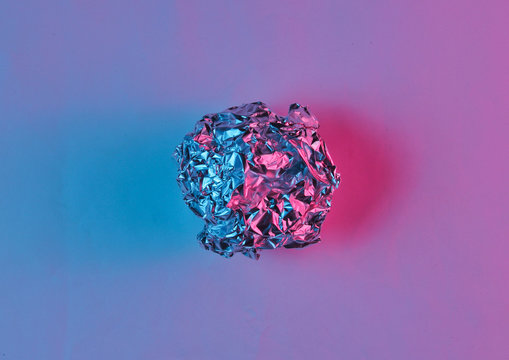 Crumpled paper ball enveloping neon blue pink light. Top view, surrealism