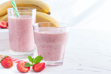 Smoothies of fresh strawberries and bananas in glass glasses on a white table, copy space
