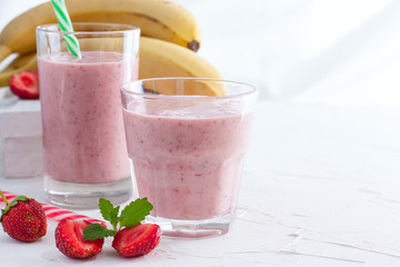 Smoothies of fresh strawberries and bananas in glass glasses on a white table, copy space