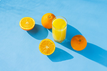 A glass of orange juice and oranges on a blue background. Concept of vitamins, tropic, summertime. Natural light. Flat lay, top view.