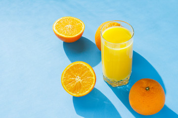 A glass of orange juice and oranges on a blue background. Concept of vitamins, tropic, summertime. Natural light. Flat lay, top view.