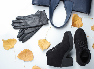 Autumn women's accessories whith fallen leaves. Leather gloves, bag, boots on a white background. Top view. Flat lay
