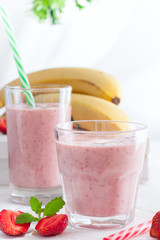 Smoothies of strawberries and bananas in glass glasses on a white table, selective focus