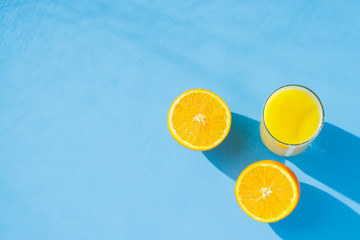 A glass of orange juice and oranges on a blue background. Concept of vitamins, tropic, summertime. Natural light. Flat lay, top view.