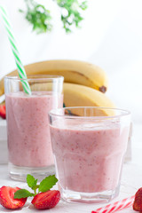 Smoothies of strawberries and bananas in glass glasses on a white table, selective focus