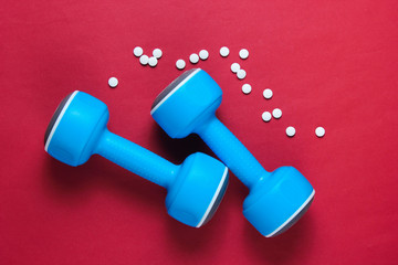 Sport concept. Dumbbells, pills on red background. Minimalism. Top view